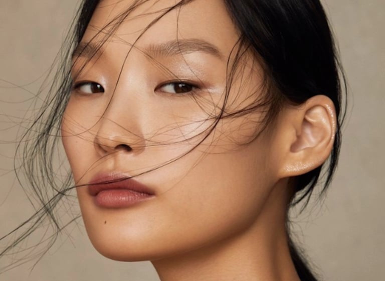 Close-up portrait of an Asian woman with a natural makeup look and wind-swept black hair.