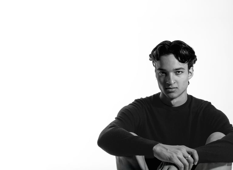 Black and white portrait of a young man in a dark sweater sitting against a white background.