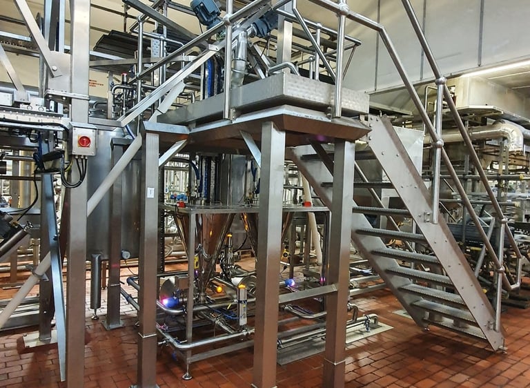 Industrial stainless steel processing machinery with metal stairs on a red brick factory floor.