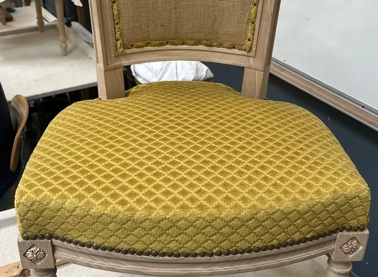 Chaise en bois clair recouverte d'un tissu jaune à motifs quadrillés, finit par des clous décoratifs