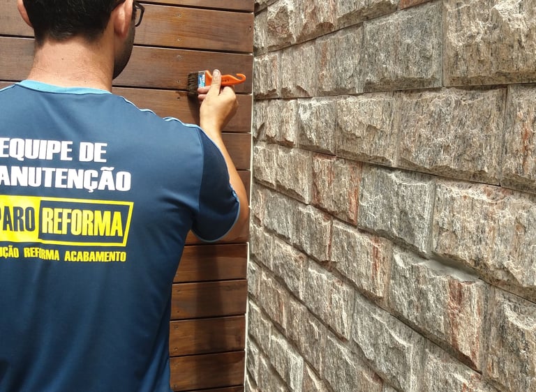 Pintor com um pincel na mao pintando uma parede de madeira ao lado de uma parede de pedras