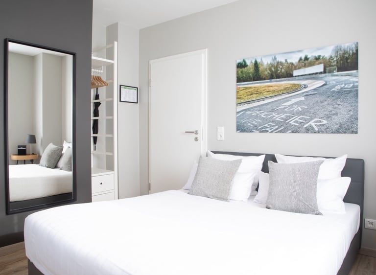 Modern minimalist bedroom with a white double bed, full-length mirror, and racetrack wall art.