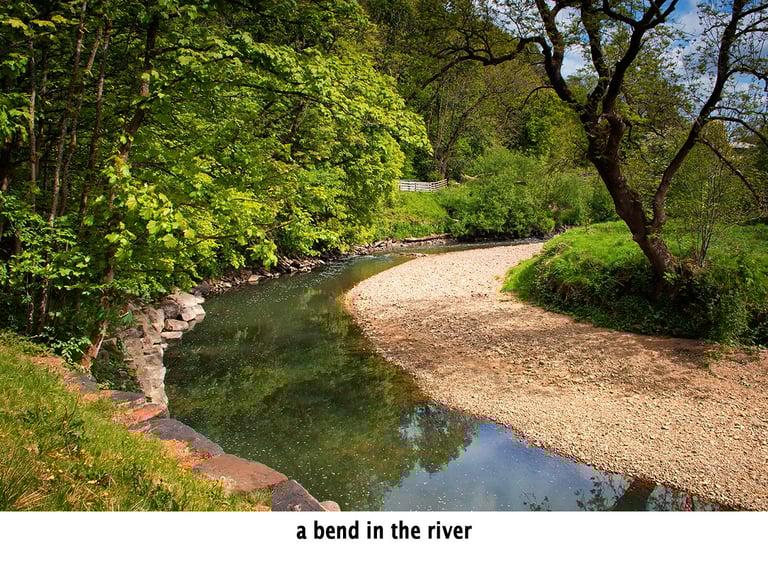 a bend in the river surrounded by trees reflected in the pendle water