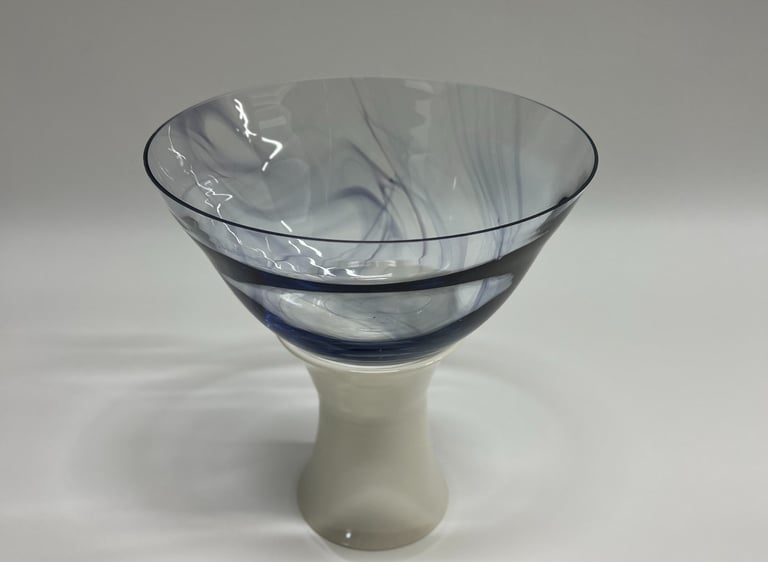 Large and wide blown glass bowl, with swirls of ink blue glass, on a white porcelain ceramic base. 