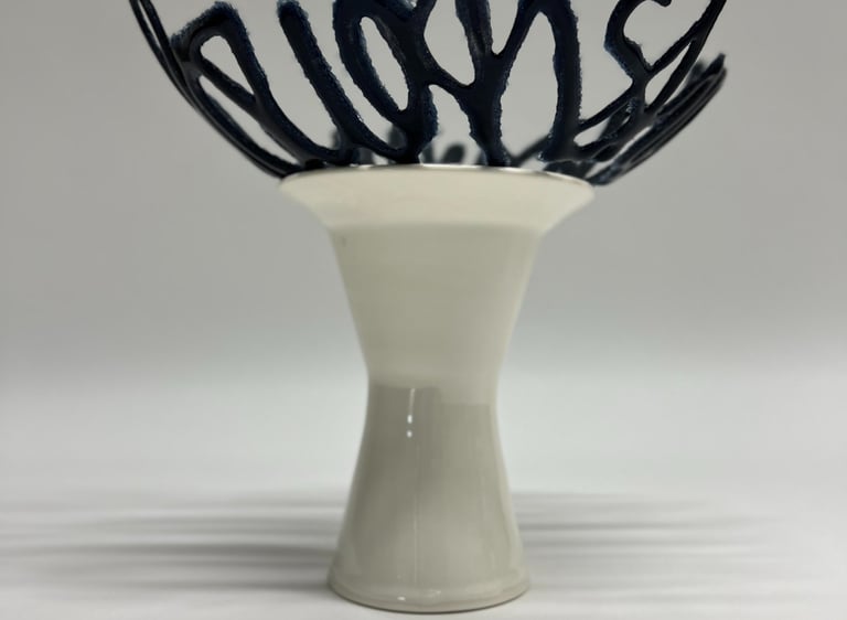 A blue glass bowl sculpture in the shape of a line of text, sitting on a porcelain ceramic pedestal