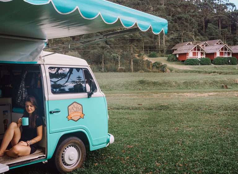 Uma pessoa sentada bebendo café dentro de uma kombi home, estacionada em um jardim.
