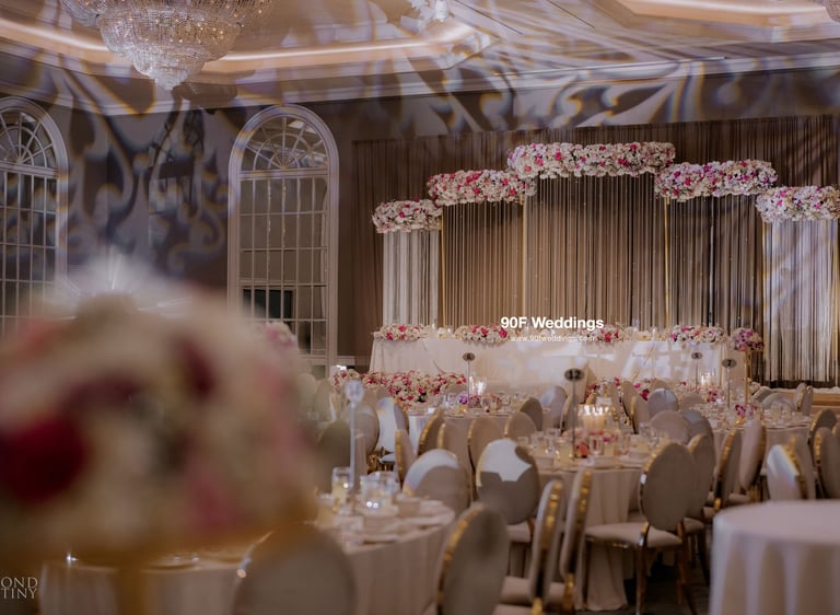 Elegant luxury wedding ballroom reception featuring a floral stage backdrop and crystal chandeliers.