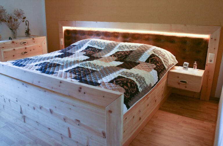 Bett aus Zirbenholz montiert beim Kunden mit gepolstertem Kopfteil und einer LED-Beleuchtung