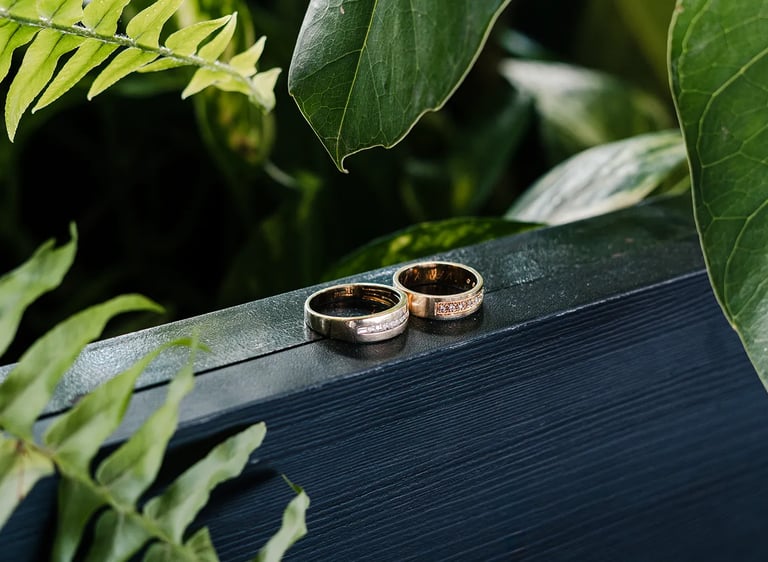 Fotografía premium de detalle de anillos de bodas reodeados de plantas en un fondo de madera azul en Quito