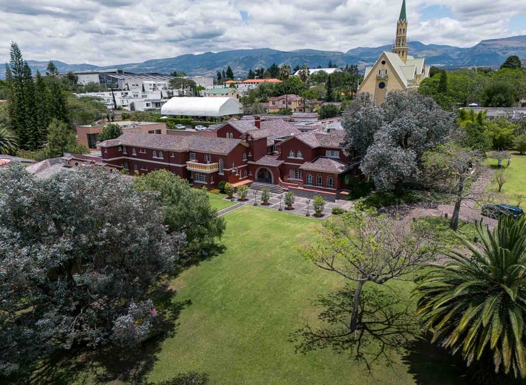 Fotografía aérea de gran casa religiosa de color rojo rodeada de hermoso jardín verde en Quito Ecuador