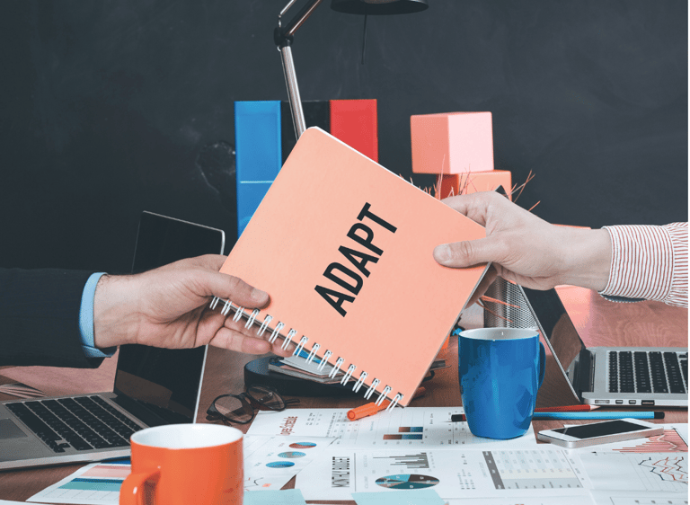 Um caderno tipo manual escrito Adapt é passado de mão em mão em uma mesa de escritório.
