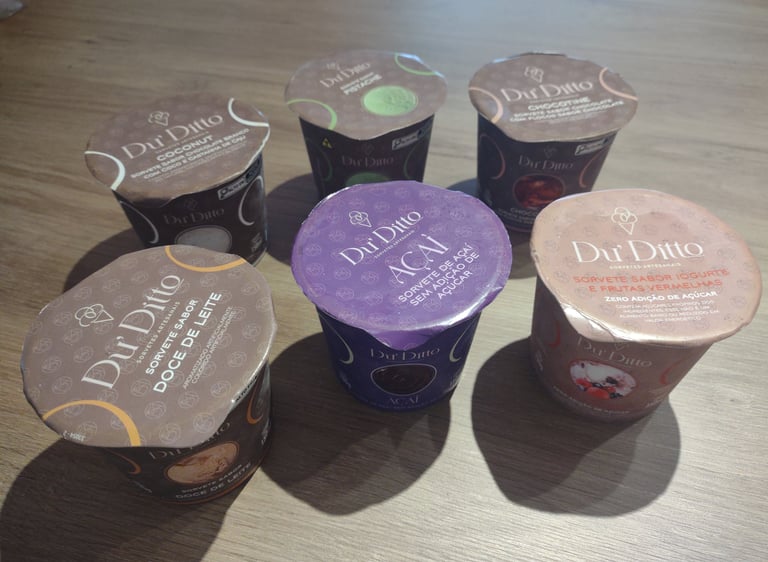 Selection of Du Ditto gourmet ice cream cups in various flavors like Acai and Dulce de Leche on a wooden surface.