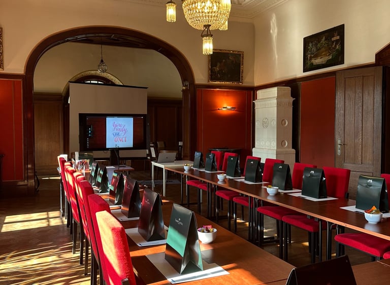 Elegant conference room with red chairs, wooden tables, and a crystal chandelier for corporate events.