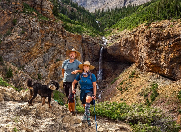 Hikers with dog on the Crypt Lake Trail beside a waterfall in Waterton Lakes National Park.
