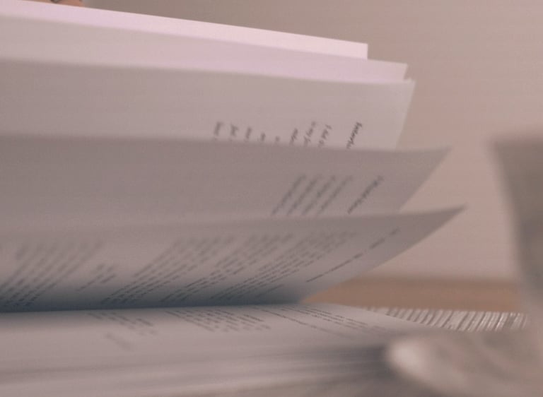 Close-up of a person's hand flipping through book pages next to a coffee cup on a table.
