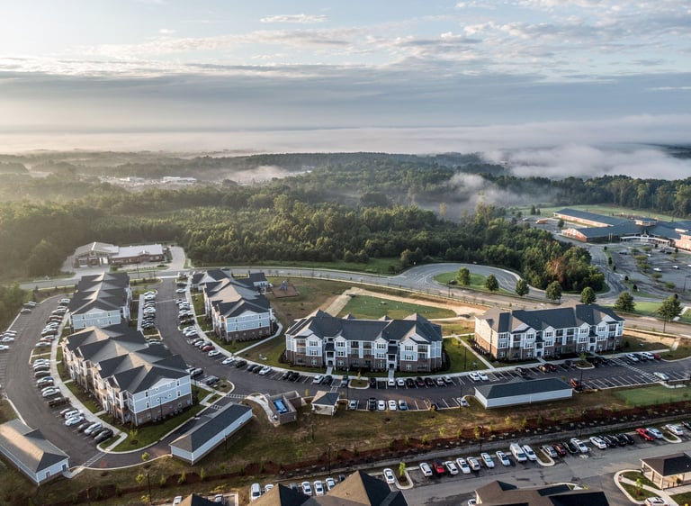 Aerial view of a completed multifamily apartment community with residential buildings, parking areas, and green space.