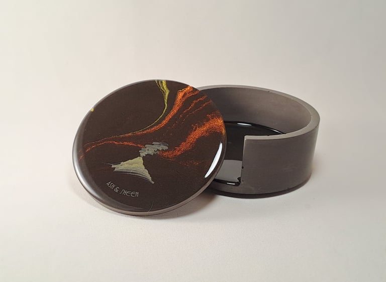 Handmade resin coaster with abstract volcano art resting against a grey gypsum holder.