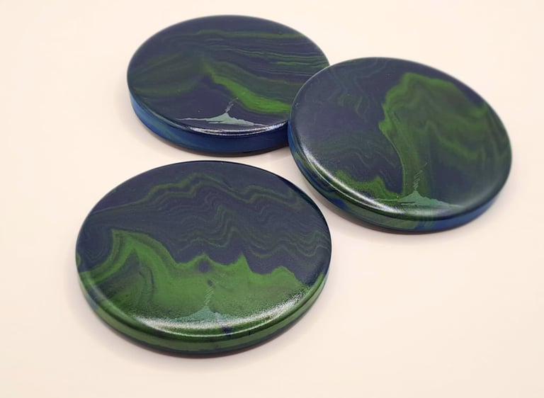 Three round handmade coasters with blue and green swirl patterns mimicking northern lights..