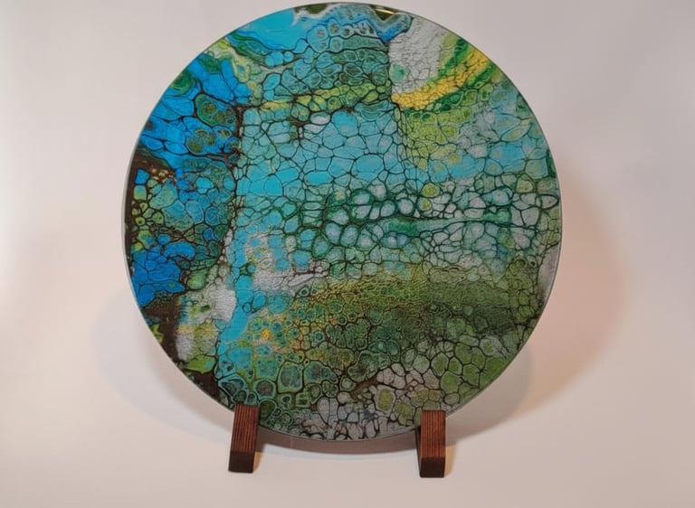 Round abstract acrylic pour painting with cell patterns in blue, green, and gold on a wooden stand.