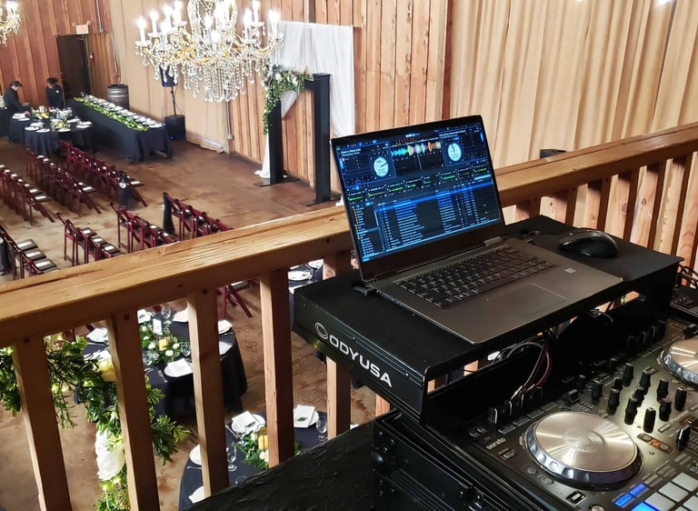 a dj booth with a laptop overlooking a wedding ceremony space from the balcony
