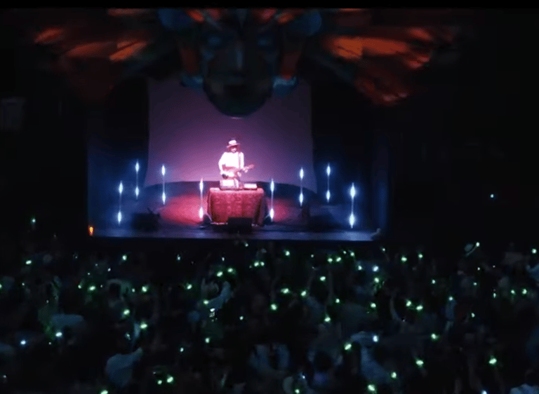 Musician performing live on a concert stage with glowing green lights from the crowd.
