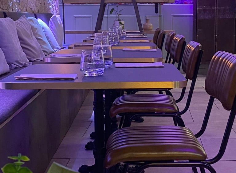 Modern restaurant dining area with leather chairs, set tables, and vibrant purple neon lighting.
