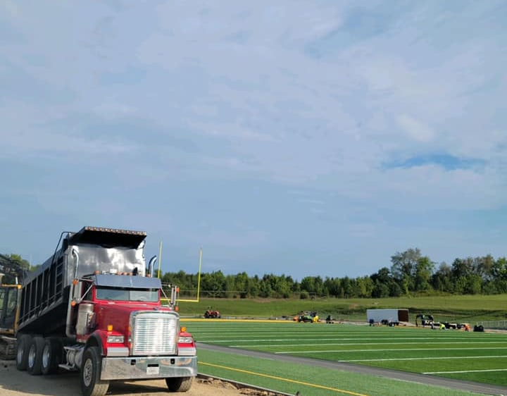a dump truck at a football field unloading material