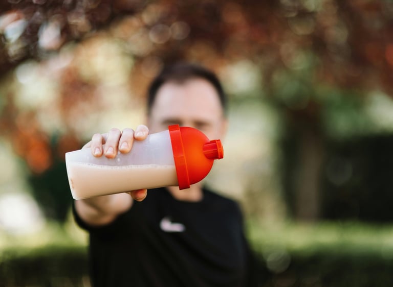 A man holding a protein shaker bottle with a red lid after an outdoor workout session.