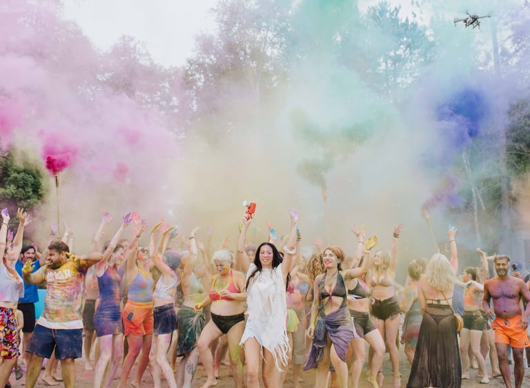 Crowd of people celebrating at a festival with vibrant clouds of purple and yellow powder.