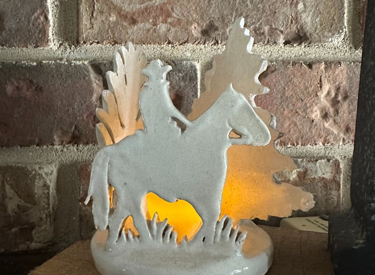 White ceramic cowboy on horse figurine with a glowing interior light set against a brick wall.