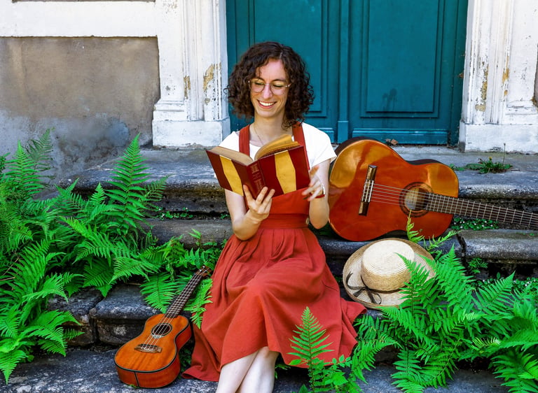 musicienne en train de lire un livre/a woman in a red dress reading on stairs with guitar beside her