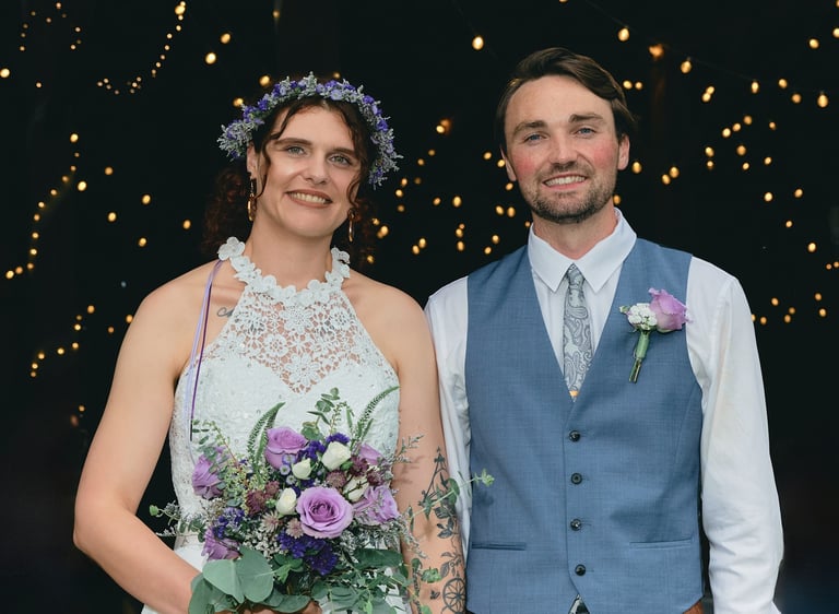 a bride holding a bouquet standing next to the groom with lights behind