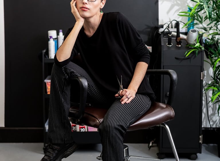 A hairdresser sits in a salon chair holding posing with a pair of scissors