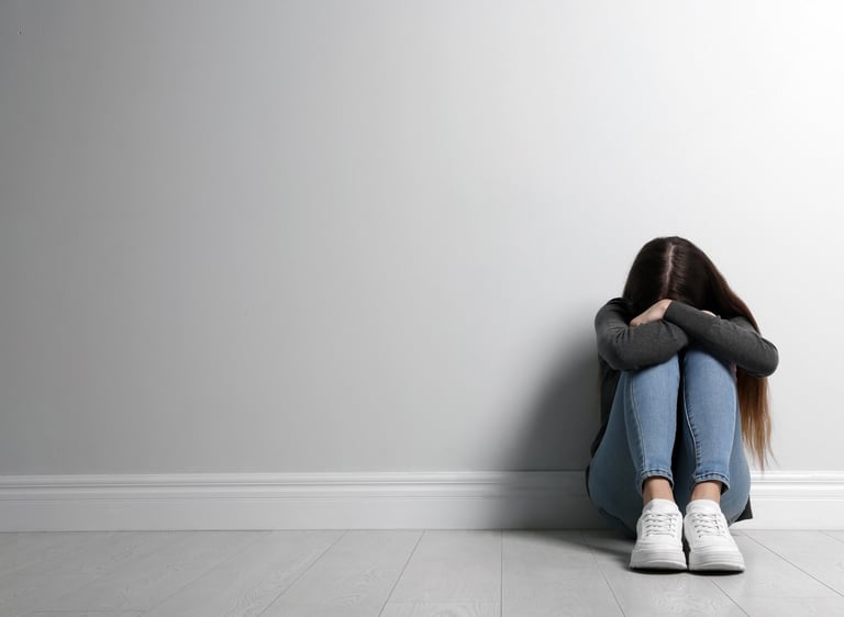 Eine Jugendliche sitzt auf dem Boden mit dem Gesicht in den Knien