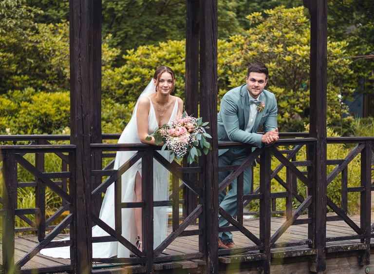 Brautpaar lehnt entspannt an einer Holzbrücke im Grünen. Hochzeitsportrait von Just Perspectives.