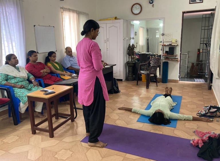 a woman in a pink shirt is standing in a room with several people during a teacher yoga class