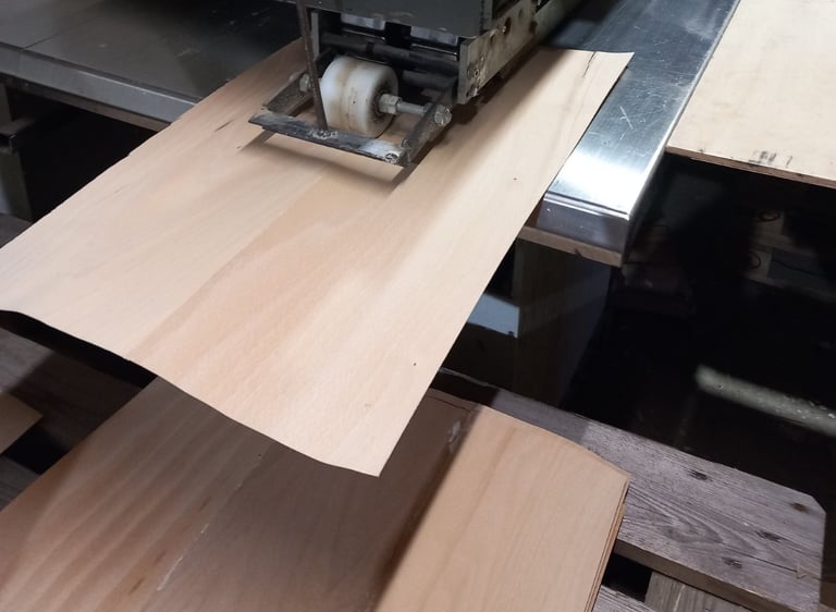 Industrial woodworking machine processing thin wood veneer sheets for furniture manufacturing.