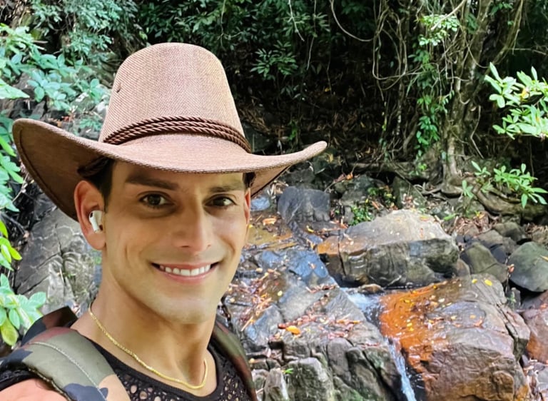 Travel writer Rick Silvia smiles at the camera wearing a cowboy hat in front of a waterfall