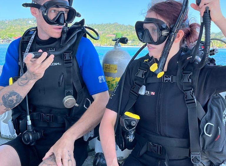 Two scuba divers wearing wetsuits and masks prepare for a dive doing a buddy check on a boat.