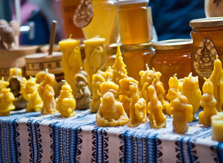 Handmade beeswax candles in various shapes displayed with honey jars at a local market.