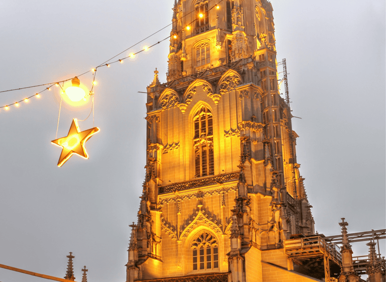 The illuminated Gothic spire of Bern Minster cathedral at dusk with festive Christmas lights and stars.