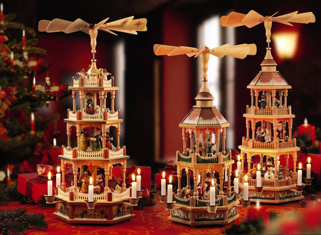 Three traditional German Christmas pyramids with lit candles and tiered wooden nativity scenes.