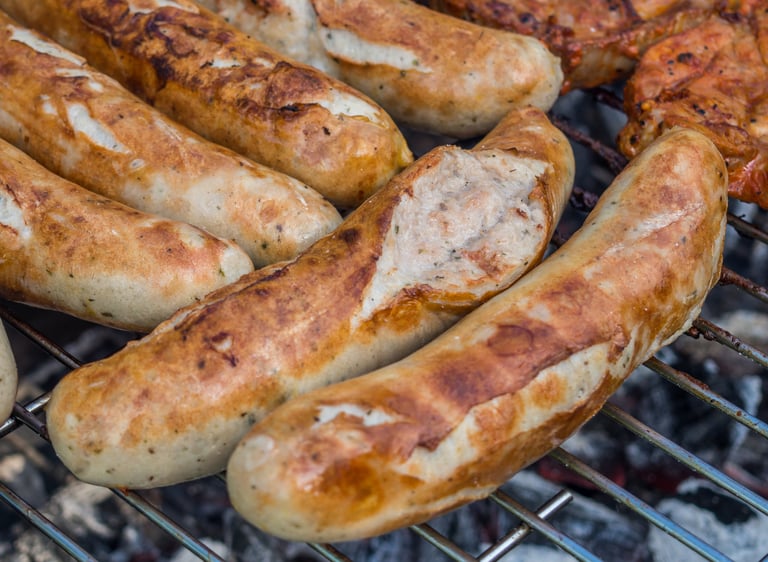 Juicy bratwurst sausages with grill marks cooking on a charcoal barbecue grill.