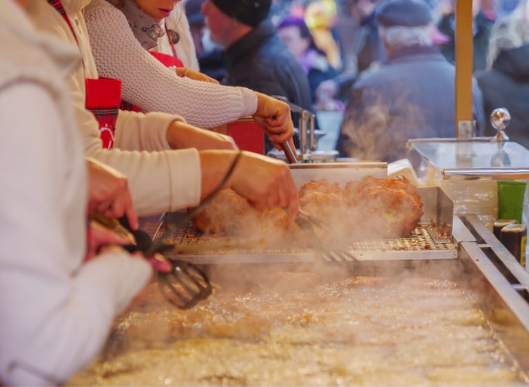 Street food vendors frying crispy potato pancakes at a busy outdoor European Christmas market stall.