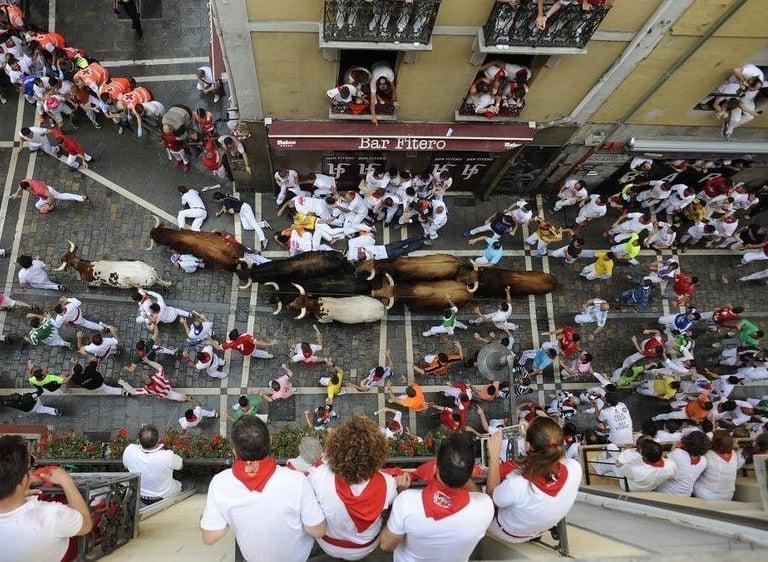 Aerial view of bulls and participants running through cobblestone streets during the San Fermin festival in Pamplona.