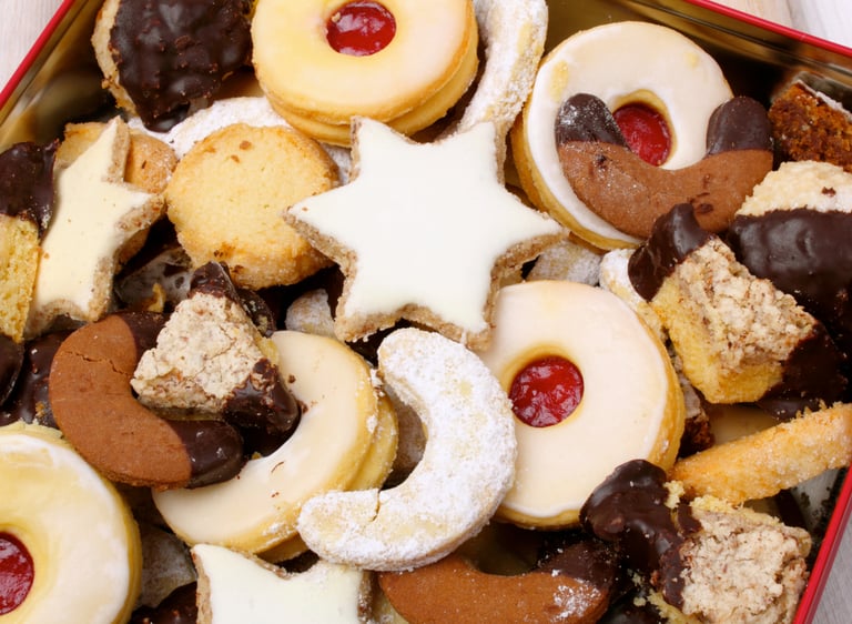 Assorted Christmas cookies including jam-filled linzer, chocolate crescents, and iced stars in a tin.