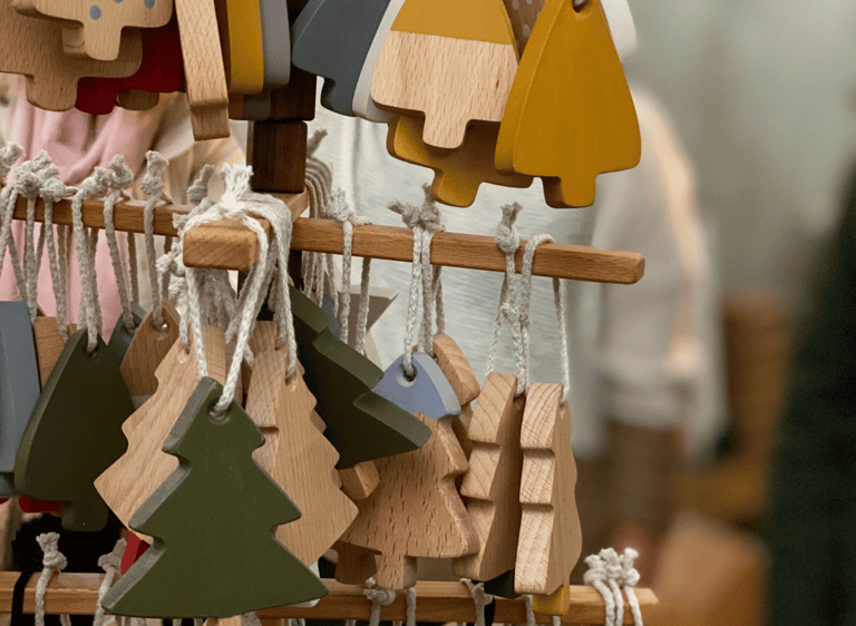 Handcrafted wooden Christmas tree ornaments in various colors hanging on a display stand at a craft market.