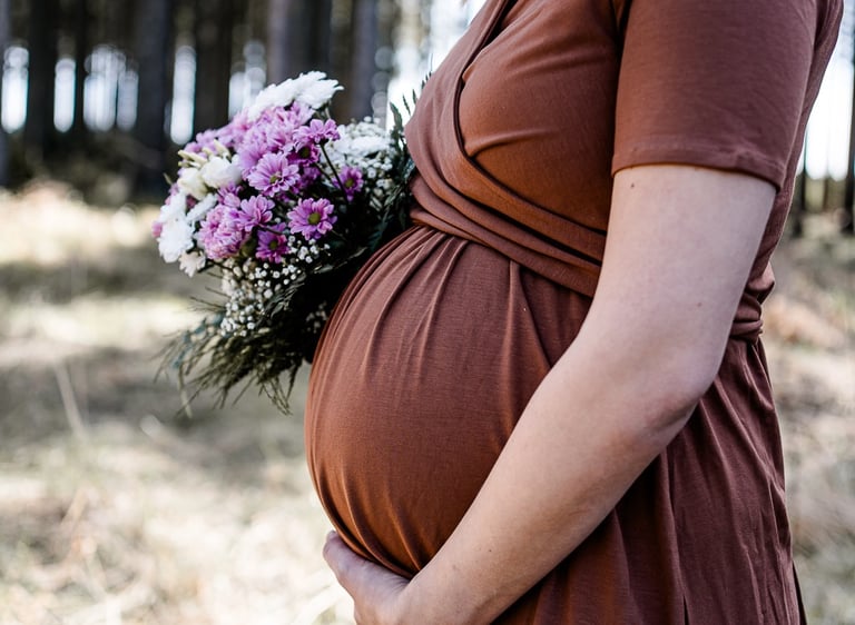 ein Babybauch an dem Blumen gehalten werden