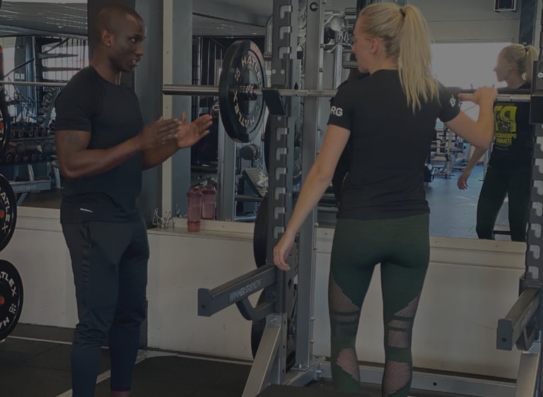 A personal trainer providing coaching to a woman performing barbell squats at a gym power rack.