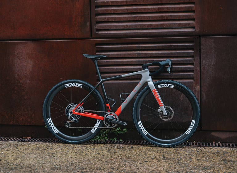 Custom OPEN gravel bike with ENVE carbon wheels leaning against a weathered metal wall.